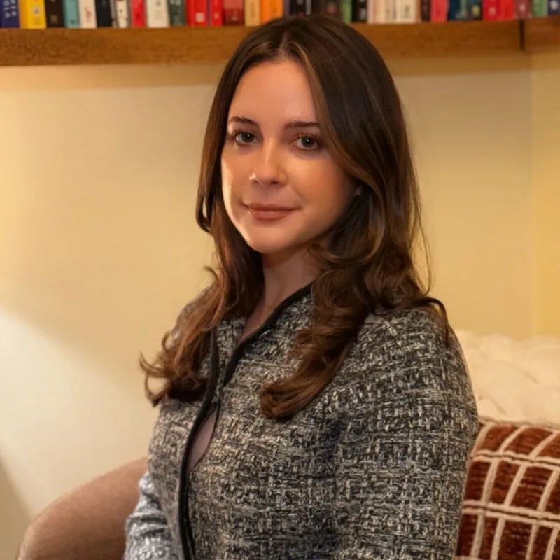 Flora Irani, Registered Psychotherapist and Clinical Director, seated in front of the practice bookshelves.